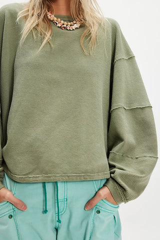 Person wearing a green ribbed sweater and light blue pants on a white background